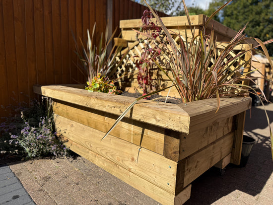 Timber sleeper planter filled with ornamental grasses and flowering plants on a patio